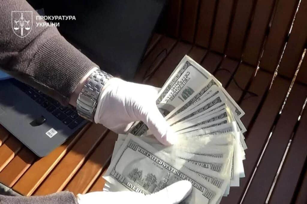 Слідчий у рукавичках тримає пачку доларів — речовий доказ хабара під час затримання полковника Нацгвардії