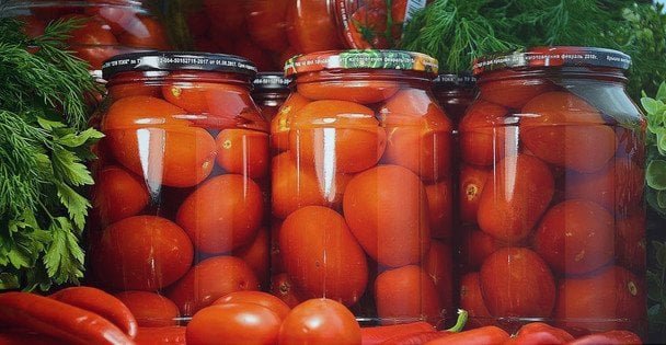 Мариновані помідори у скляних банках з часником та зеленню для заготівлі на зиму